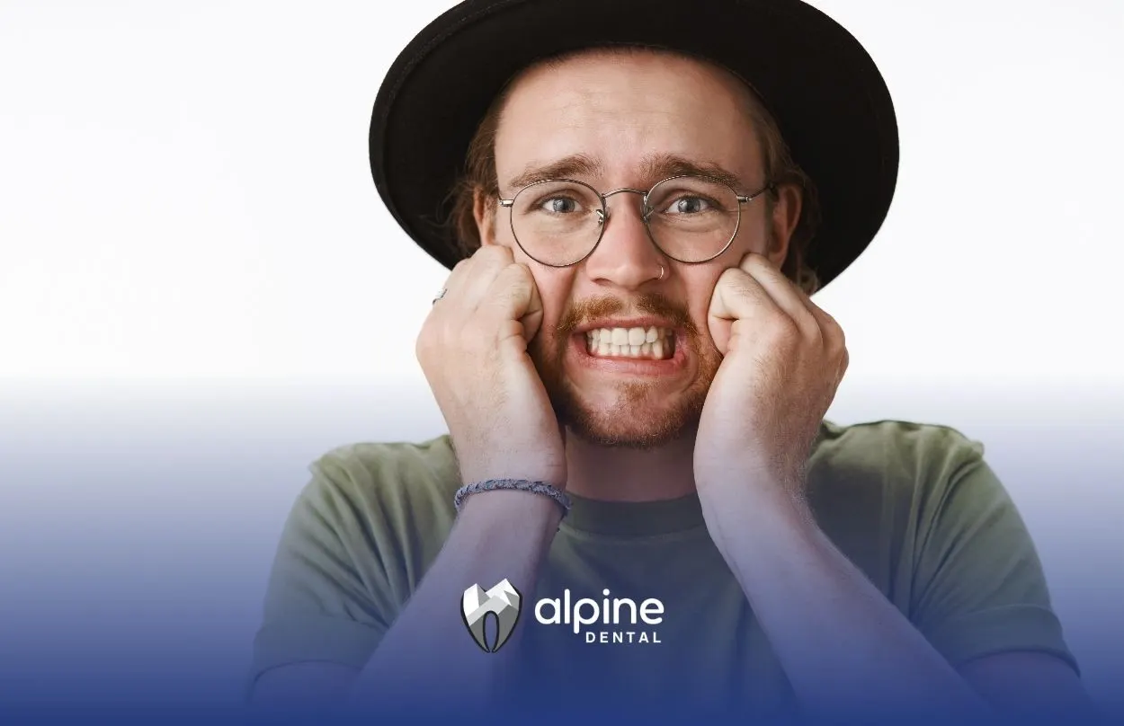 Person wearing hat showing discomfort while clenching his teeth, representing tooth pain or sensitivity from a cracked tooth.
