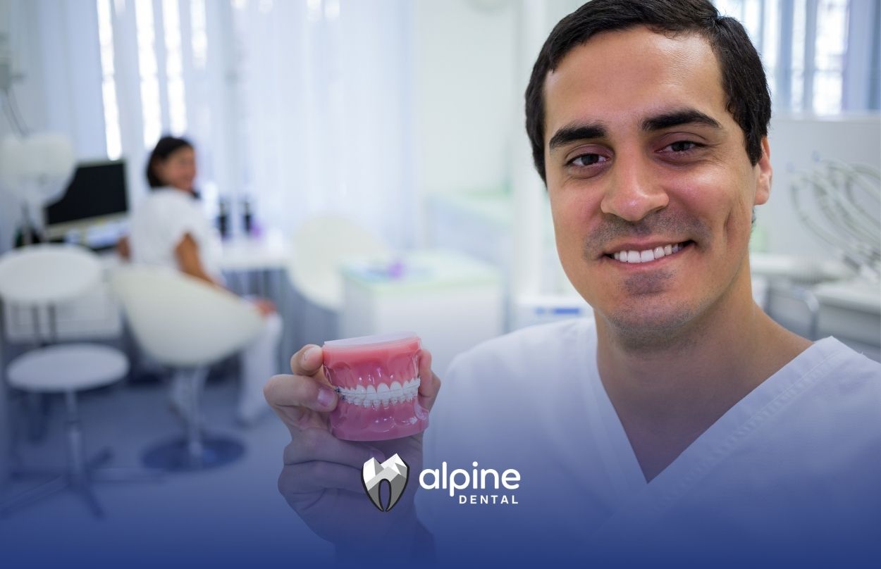 Dentist holding a dental model showing dentures and tooth restoration options during a consultation in a modern clinic.