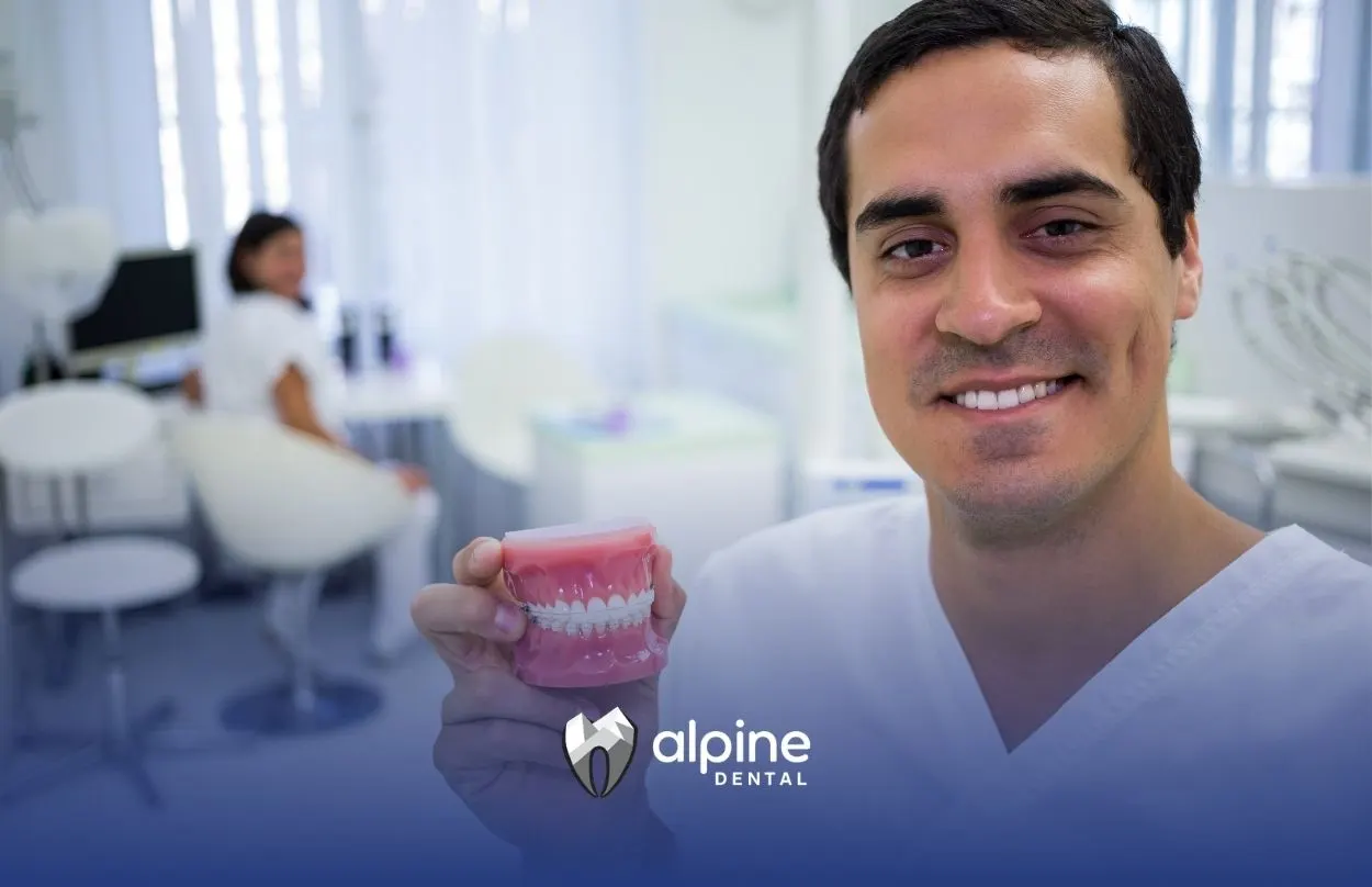 Dentist holding a dental model showing dentures and tooth restoration options during a consultation in a modern clinic.