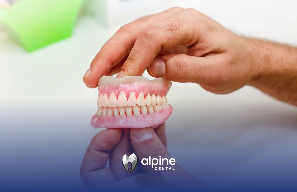 Hands hold a set of dentures, showing artificial teeth and gums up close during a dental fitting and evaluation process.