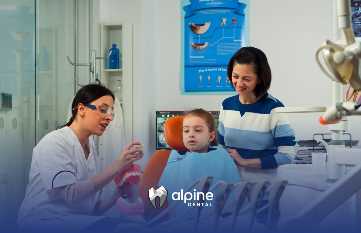 Child receiving dental care while a dentist explains treatment steps to a young girl and parent in a modern clinic setting.