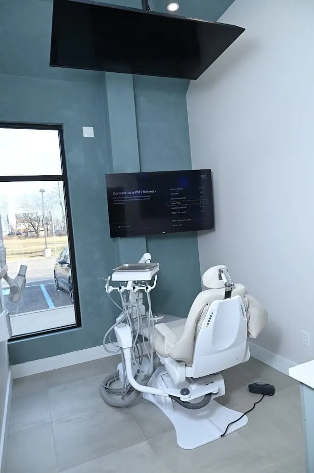 Treatment room with a blue accent wall, window and wall-mounted TV at Alpine Dental in Jackson